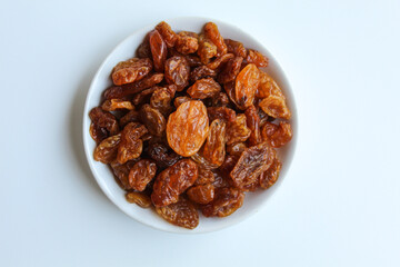 Raisins in small white plate, isolated on white background