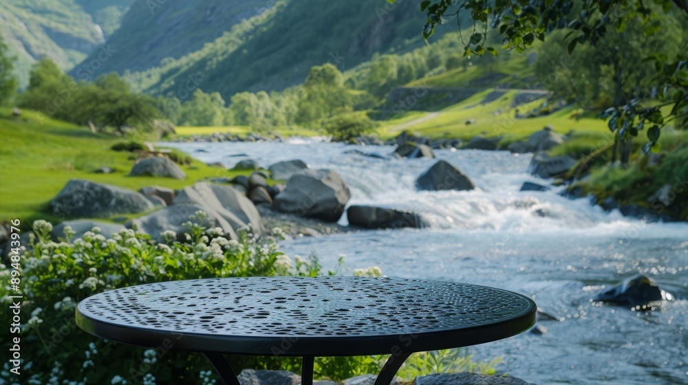 Aufkleber A wet table sits on the edge of a green meadow overlooking a rushing river. The surrounding mountains are visible in the distance.