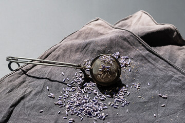 Tea strainer with lavender buds on dark cloth background.