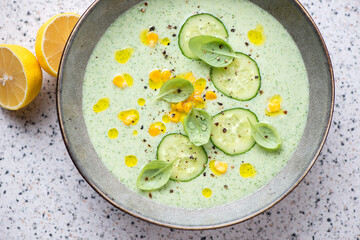 Chilled soup made of cucumber and topped with sweet corn, horizontal shot on a light-grey granite background, high angle view, middle closeup