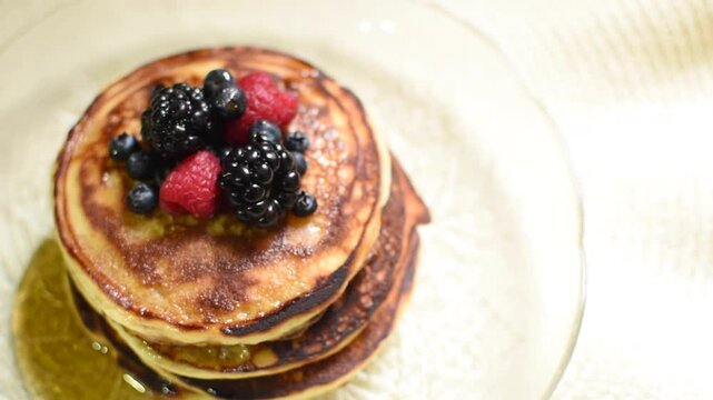 Toma cenital de un plato de hotcakes o panqueques con miel y frutos rojos como mora azul y frambuesa 