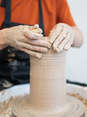 Close-up of a potter's hands making a ceramic vase on a potter's wheel. Vertical photo. 