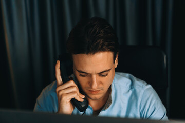 Smart businessman calling with telephone office for consulting business paragraph dynamic data marketing analysis plan surrounded paper sheet and pc monitor report at home office at night. Pecuniary.