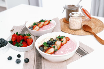 Presented by fruits putting yogurt toppings with strawberry, berry, oats, raisins and chia seed decorated by peppermint in white blow. Pink background. Set of healthy dairy product choice. Pecuniary.