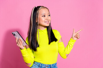 Photo of smart pretty girld ressed yellow shirt hold smartphone look directing at sale empty space isolated on pink color background