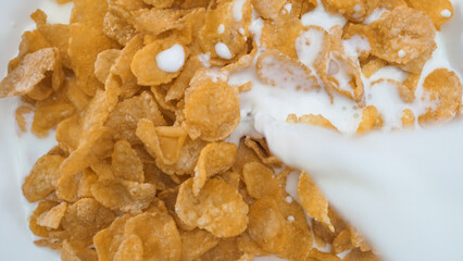 Close up of a white bowl of cereal with milk being poured into it. Macrography of white milk pouring in to bowl with yellow cornflake and splashing milk with isolated white background. Pabulum.