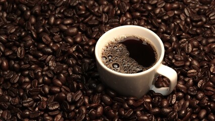 Top view of coffee or espresso with piles of coffee beans. Close up of fresh roasted coffee bean scatter around wooden table with cup of americano and aromatic stream and smoke from seed. Comestible.