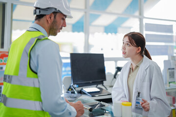 A female pharmacist is talking with a construction worker who needs medicine for pain and...