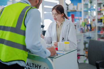 A female pharmacist is talking with a construction worker who needs medicine for pain and discomfort. Pharmacist in a pharmacy with medicines on shelves