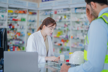 Obraz premium A female pharmacist is talking with a construction worker who needs medicine for pain and discomfort. Pharmacist in a pharmacy with medicines on shelves