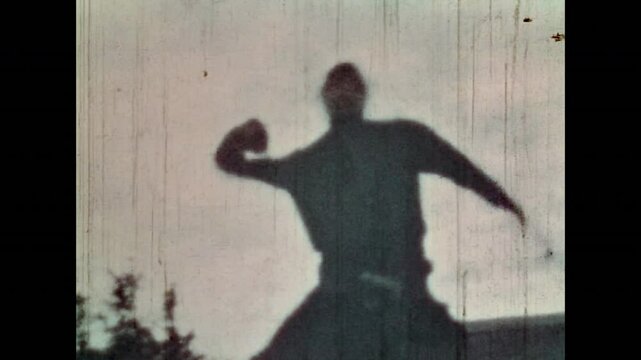 Male fighter breaking brick on head on blue sky outdoors. Aggressive man demonstrating anger, aggression. Old nostalgic film. Martial power. Furious conflict. Vintage color archive. Retro 1960s