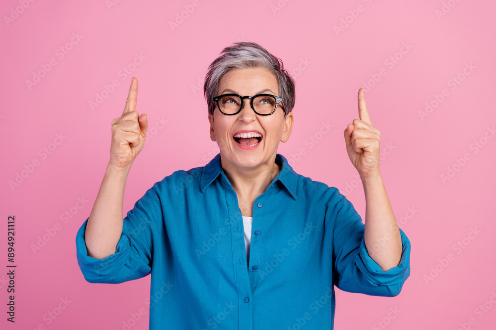 Sticker Photo portrait of attractive senior woman look point up excited empty space dressed stylish blue clothes isolated on pink color background