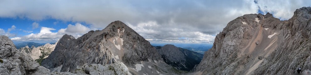 Obraz premium Panoramic view of the Slovenian Alps from a hiking trip and via ferrata to the top of Grintovec mountain on a hot summer day. Stunning alpine landscapes and challenging trails.