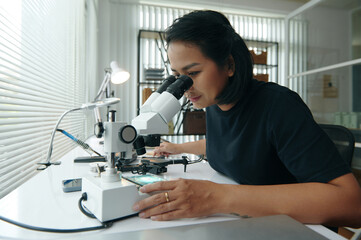 Master using microscope at her workplace while examining details of drone during repair