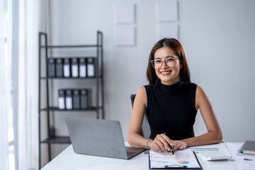 A woman is sitting at a desk with a laptop and a stack of papers