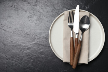 Stylish cutlery, plate and napkin on black table, top view. Space for text