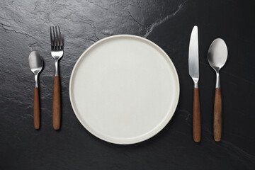 Stylish cutlery and plate on black table, flat lay