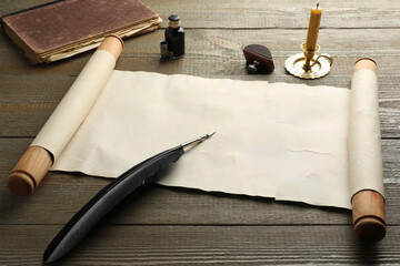 Sheet of old parchment paper, wax stamp, black feather, inkwell, candle and vintage book on wooden...