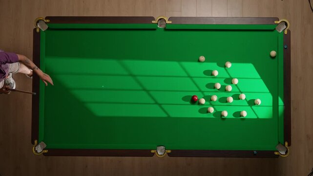 Top view full shot of russian billiard green cloth table with white balls being hit by red ball, person hitting the ball pyramid with cue.