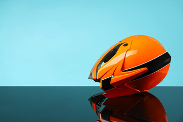 Modern motorcycle helmet with visor on mirror surface against light blue background. Space for text