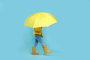 Little girl with yellow umbrella on light blue background