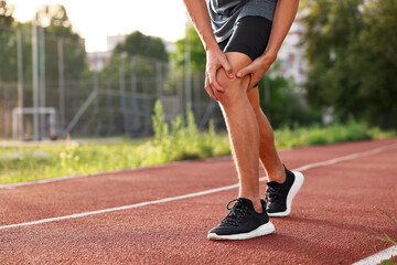 Obraz premium Sportsman with leg injury suffering from knee pain at stadium, closeup. Space for text