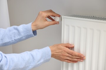 Woman adjusting temperature of heating radiator indoors, closeup