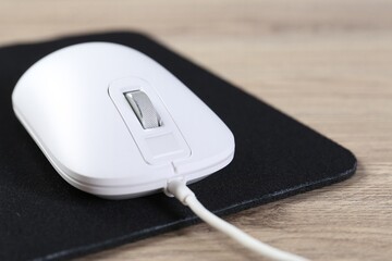 White computer mouse and black mousepad on wooden table, closeup