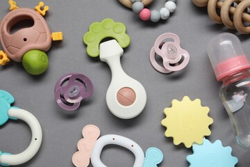 Colorful rattles, bottle and pacifiers on gray background, flat lay. Baby accessories