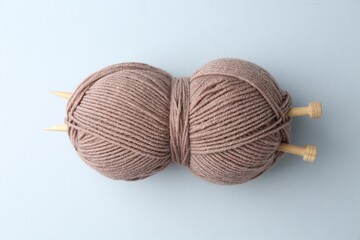 Brown yarn with knitting needles on light grey background, top view