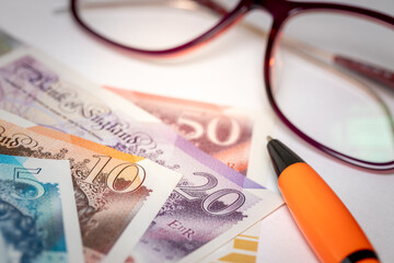 British pounds money on the desk next to women's glasses, white sheet of paper and pen, concept, payment of bills, installments and loans, rising costs of household budget in the UK