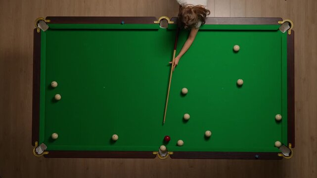 Top view shot of russian billiard green cloth table with red and white balls, woman hitting the balls with cue.