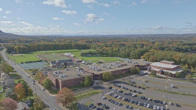 Southington High School in Connecticut, drone video showing front of building with parking lot and sports fields and tennis courts.