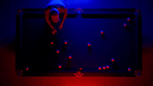 Hobby and leisure concept, billiard club scene shot. Top view of Russian billiard table in neon blue red light, man playing billiards.