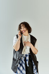 A woman in a leather vest and pearl necklace laughs while talking on the phone.