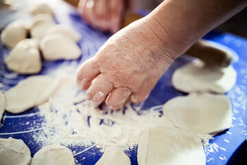 A Person's Hand Preparing Dough for Dumplings on a Blue Mat