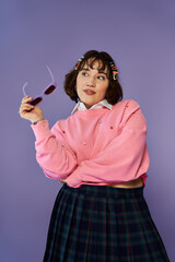 Obraz premium A woman in a pink sweater and plaid skirt looks thoughtfully at sunglasses in her hand.