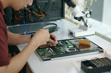 Technician examining motherboard of laptop with magnifier while sitting at his workplace
