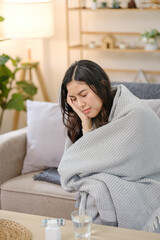 A woman is wrapped in a blanket and is sitting on a couch