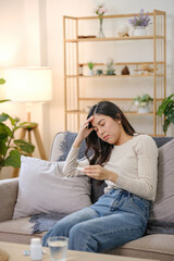 A woman is sitting on a couch with her head on her hand