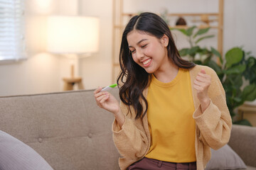 A woman is sitting on a couch with a pregnancy test in her hand