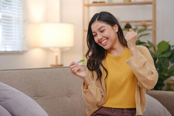 A woman is sitting on a couch with a green pregnancy test in her hand