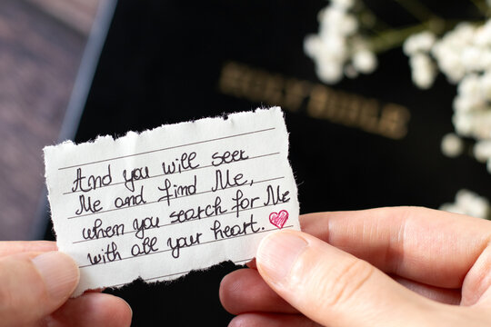 Hand holding handwritten Christian quote to seek God with all heart. Close-up. Biblical concept of love, obedience, humility, and faith in Jesus Christ.