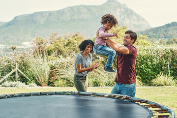 Parents, trampoline and boy jump in outdoor, playing and father helping in backyard of home. Son, family and kid energy for fun activity in childhood, garden and bounce movement for bonding together