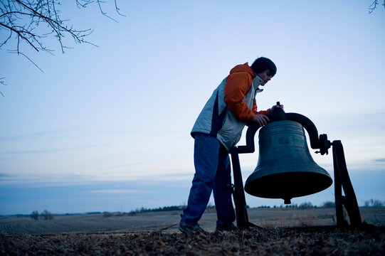 Silhouette of a teenage boy ringing an old bell on a farm in the vast counryside in Nebraska, USA; Cortland, Nebraska, United States of America