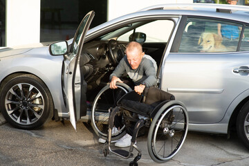 Paraplegic man assembles his manual wheelchair from the front seat of his car; Boynton Beach, Florida, United States of America
