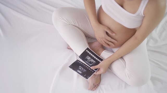 A portrait of happy Asian pregnant woman in bedroom at home with baby ultrasound. Having a baby. Family people lifestyle. Mom love.