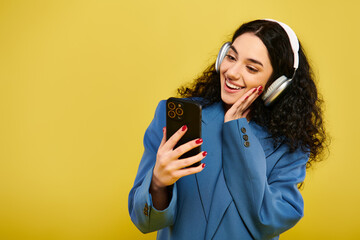 Naklejka premium A young brunette woman, with curly hair, wearing headphones, holding a cell phone, lost in music.