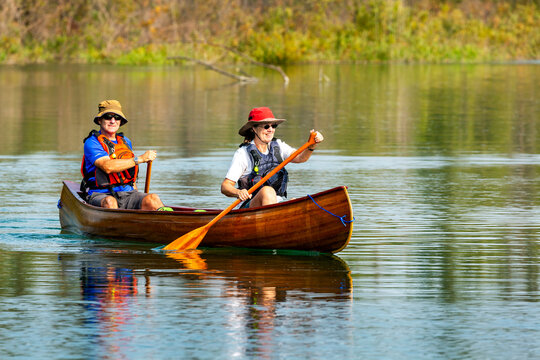 Female and male canoeists on a lake paddling with refection in the lake; Calgary, Alberta, Canada