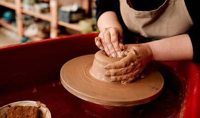 Hands, clay and pottery wheel in studio for ceramics, shape and craft into bowl or cup with spinning. Woman, mud and machine for potter in workplace for creative art, process and handmade production